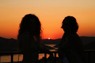 Silhouette women standing against orange sky during sunset