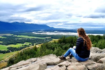 Rear view of woman sitting on rock against sky