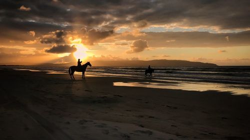 Silhouette man standing on beach against sky during sunset