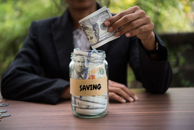 Midsection of businessman putting money in container with saving text