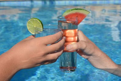 Cropped image of hand holding drink at swimming pool