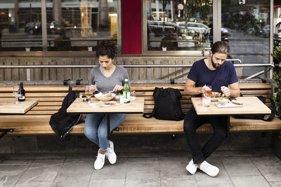 Full length of man and woman having food at sidewalk cafe