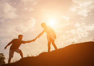 Low angle view of couple holding hands while standing on hill against sky at sunset