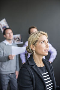 Mid adult businesswoman looking away with colleagues discussing in background