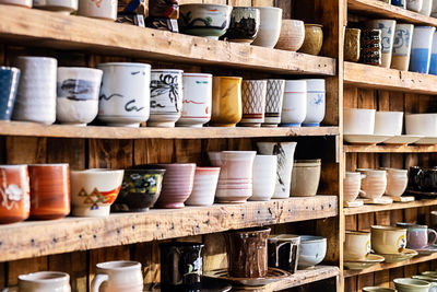 Various pottery ceramic displayed on wooden shelves at store.