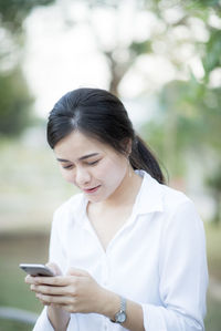 Young woman using mobile phone while standing at park