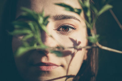 Close-up portrait of young woman with plant in foreground