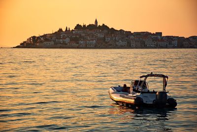 Boat sailing on sea against buildings in city at sunset