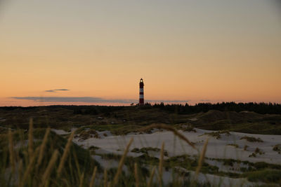 Lighthouse on field against sky during sunset