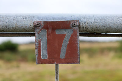 Close-up of rusty sign on field against sky