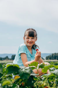 Girl sitting in field and holding strawberries in her hands
