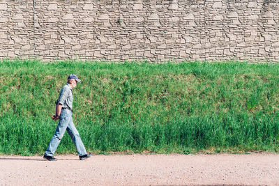Full length side view of senior man walking against wall during sunny day
