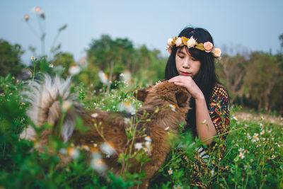 Woman wearing flowers while sitting with dog on field 