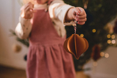 Midsection of girl holding home made christmas ornament indoors