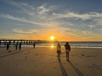 Silhouette people walking at beach against sky during sunset