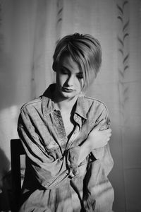 Young woman looking down while sitting on chair at home