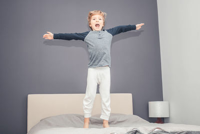 Full length portrait of boy jumping on bed at home