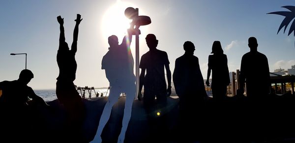 Silhouette people at beach against sky during sunset