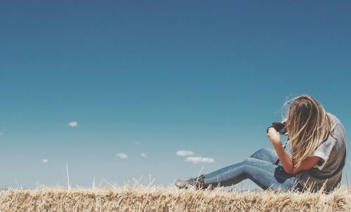 Side view of woman sitting on landscape against blue sky