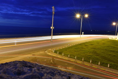 Light trails on road by sea against sky at night