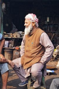 Full length of man looking away while sitting against store