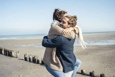 Boyfriend embracing girlfriend while picking up on beach during weekend