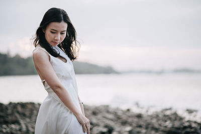 Young woman looking away while standing at beach during sunset