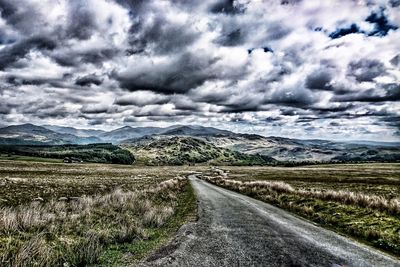 Road by landscape against storm clouds