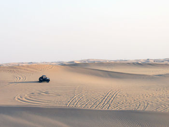 Beach buggy on sand dune in desert against clear sky