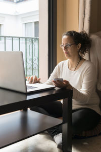Woman using laptop at table while sitting by window