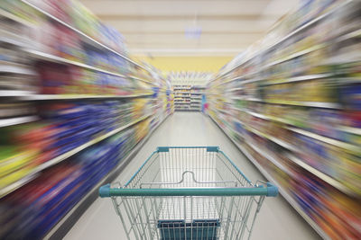 Shopping cart amidst racks in supermarket