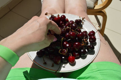 Midsection of woman eating cherry in plate