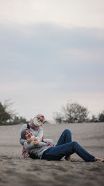 Friends relaxing on sand against sky