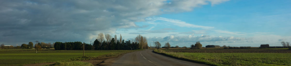 Panoramic view of road amidst field against sky