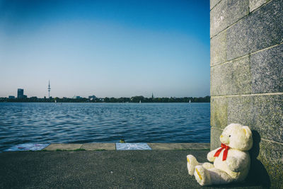 Swan on river by cityscape against clear blue sky