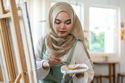 Portrait of young woman standing against window