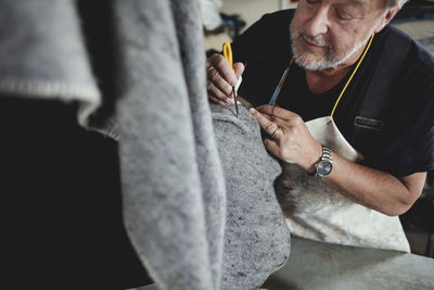 Close-up of senior craftsperson working on gray fabric at workshop