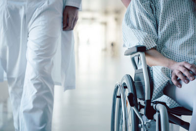 Midsection of male doctor walking with female patient in wheelchair at hospital