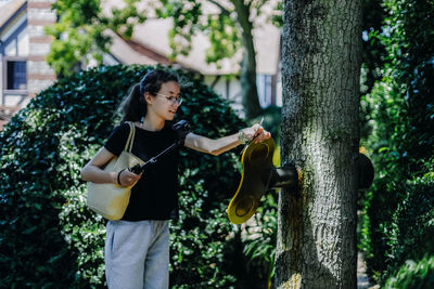 Portrait of teenage with a camera on a stick turns a large golden key sticking out of a tree trunk