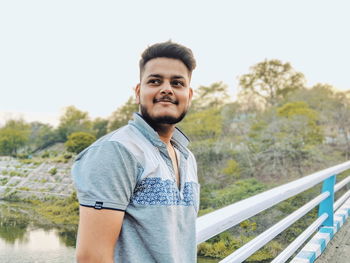 Portrait of young man standing against railing