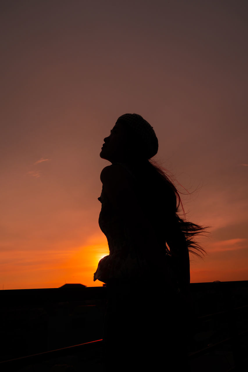 SILHOUETTE WOMAN STANDING AGAINST ORANGE SUNSET SKY