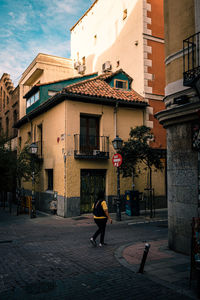 Rear view of woman walking on footpath amidst buildings in city