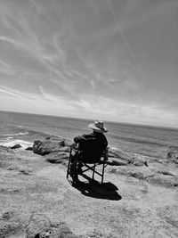 Lone man sitting in chair on cliff's whale watching against sky