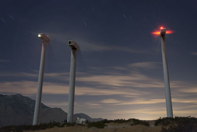 Low angle scenic view of moving wind turbines against star trails on field