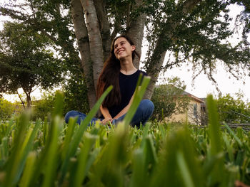 Smiling woman sitting on field against trees