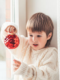 Kid with red decorative ball for christmas tree. boy in cable-knit oversized sweater. new year.