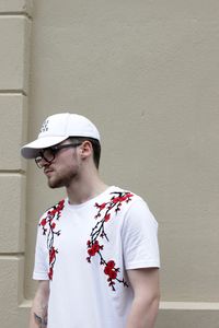 Young man wearing cap while standing against wall