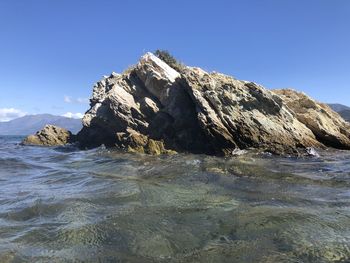 Rock formations in sea against clear blue sky