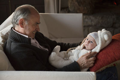 Side view of grandfather and baby sitting at home