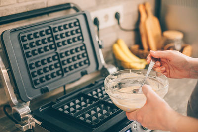 Cropped hands of woman with waffle batter in kitchen